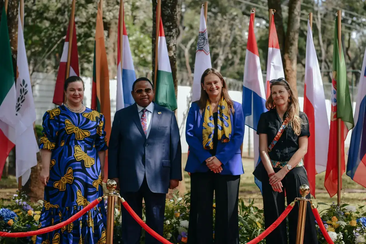 Four guests standing before a row of national flags behind red rope stanchions