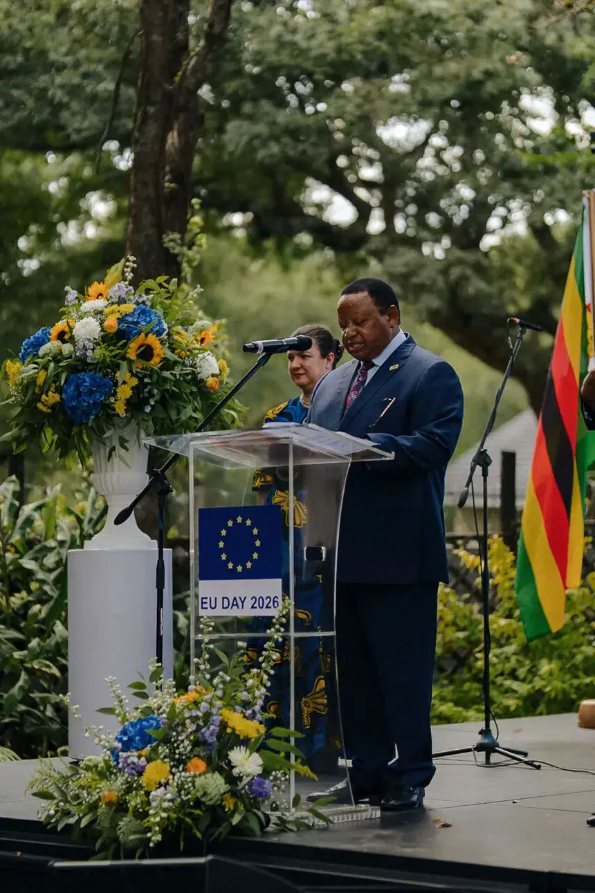A speaker at a podium dressed with blue and yellow florals, beside a national flag